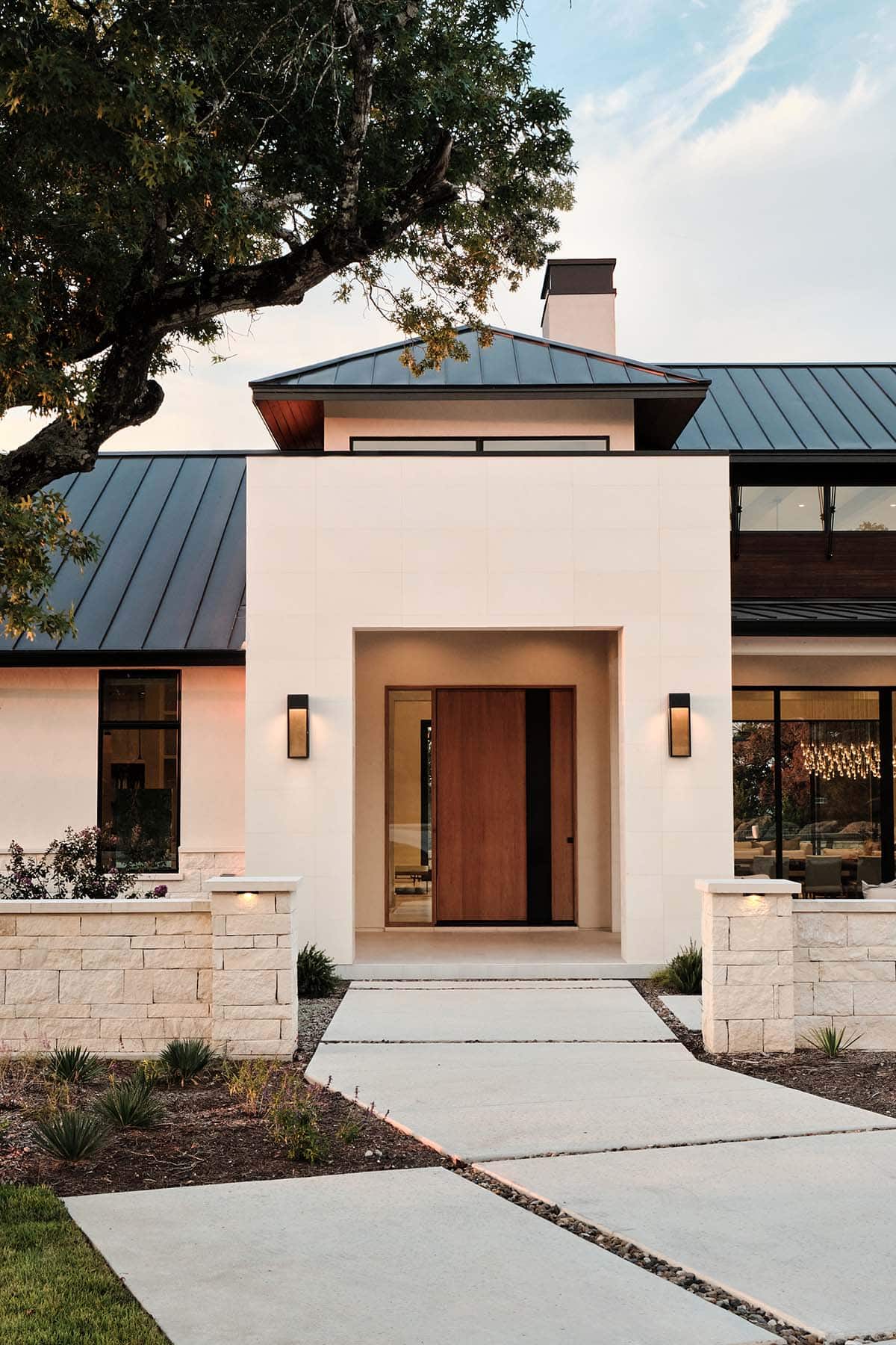Modern home entry with oversized wood pivot door, stucco facade, and stone walls at dusk