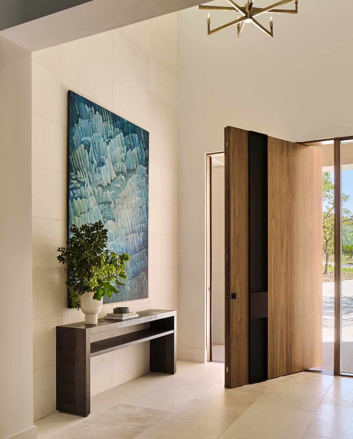 Bright foyer with large-scale blue abstract artwork, dark console table, and wood pivot door