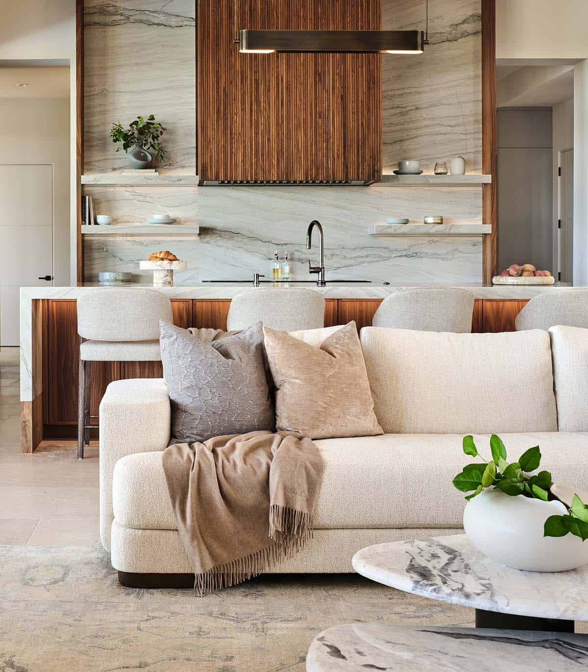 Living room sofa with neutral pillows facing marble kitchen backsplash and fluted wood range hood
