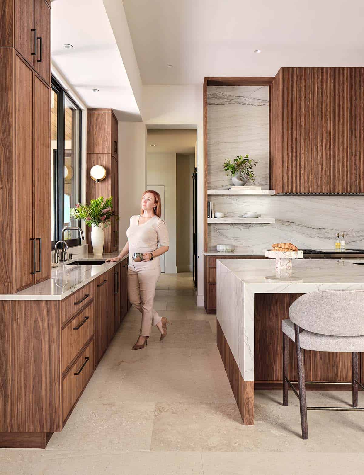 Luxury kitchen with walnut cabinetry, marble slab backsplash, fluted wood range hood, and stone tile floors