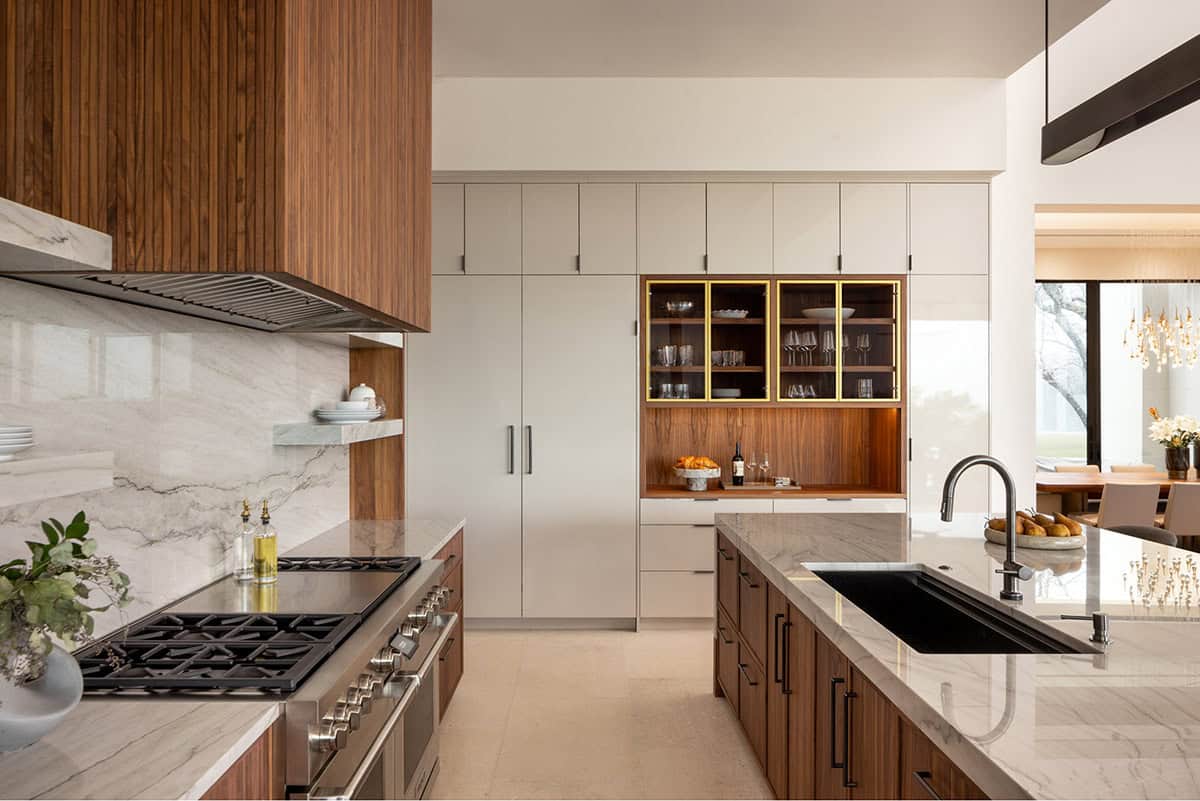 Organic modern kitchen with walnut and white cabinetry, marble countertops, professional range, and gold-framed display cabinet