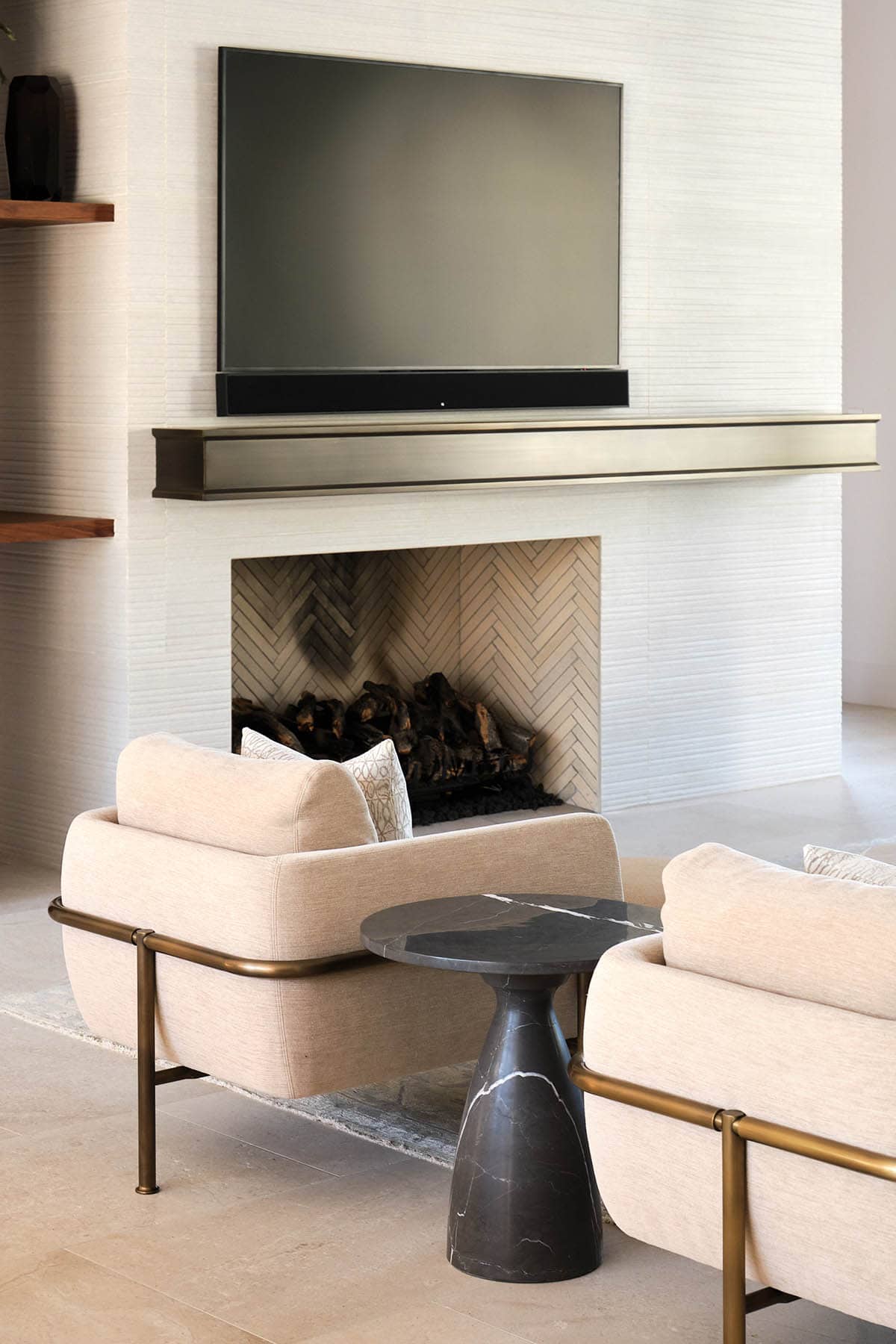 Living room fireplace with herringbone tile firebox, brass mantel shelf, and cream chairs with brass frames