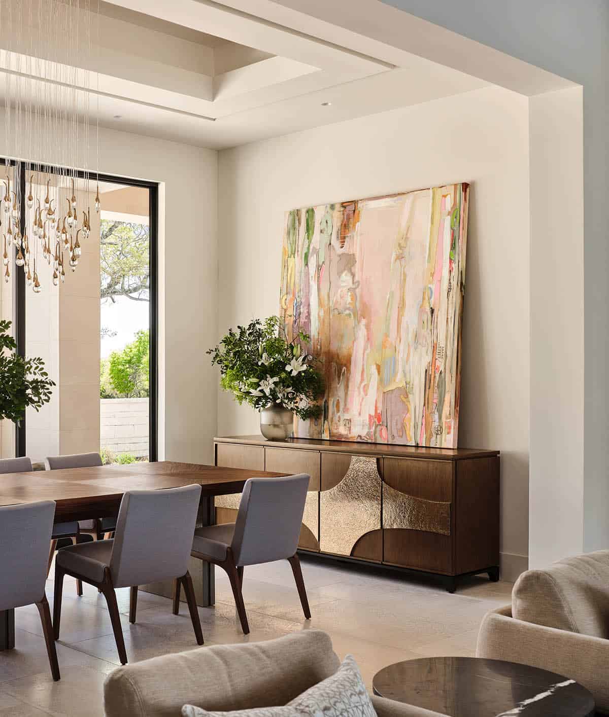 Dining room with walnut table, gray upholstered chairs, sculptural crystal chandelier, and large abstract painting