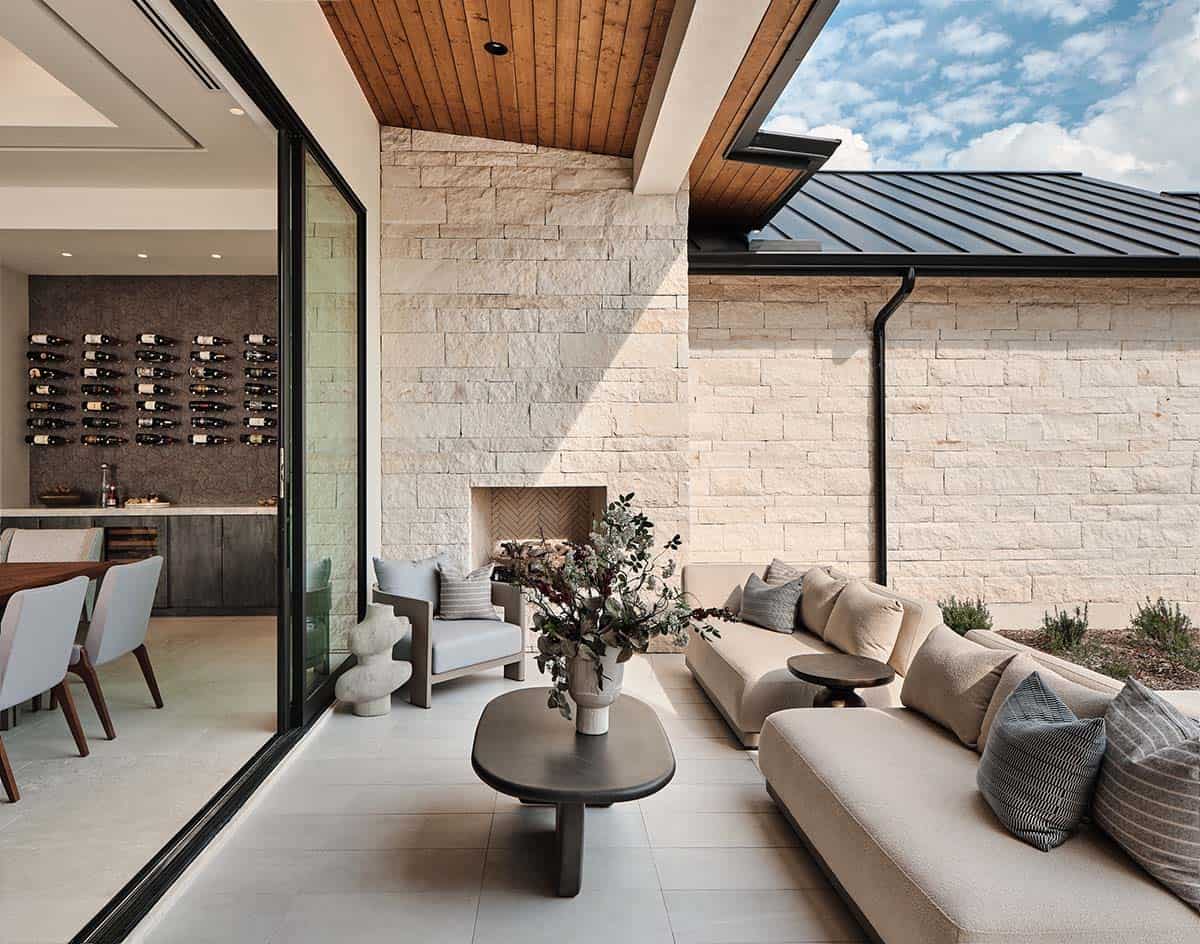 Covered outdoor living area with limestone walls, herringbone fireplace, neutral sectional, and dark metal roof