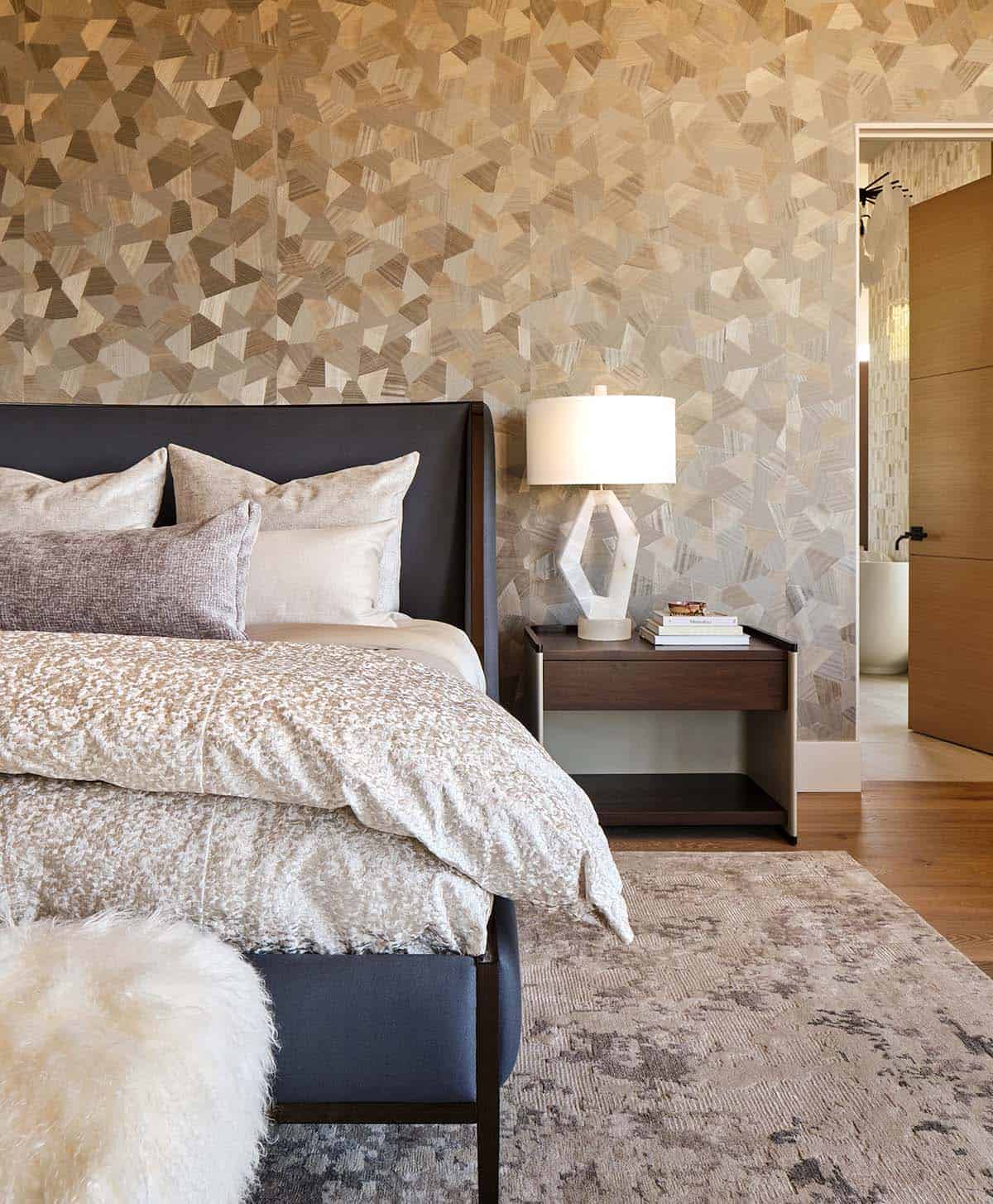 Primary bedroom detail with geometric wallpaper, dark leather headboard, and sculptural white table lamp