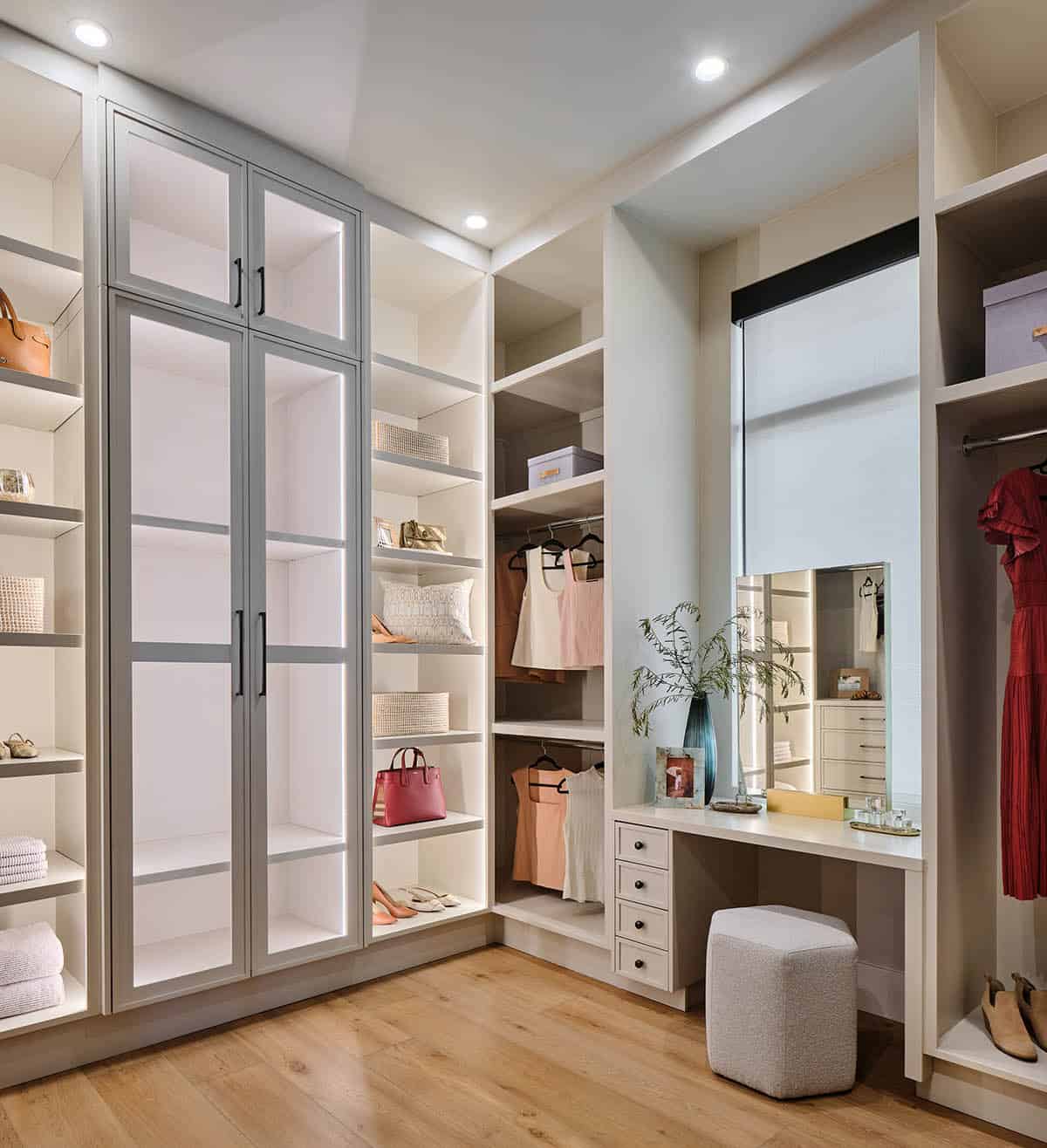 Walk-in closet with illuminated glass-front wardrobe, built-in shelving, and vanity with makeup mirror