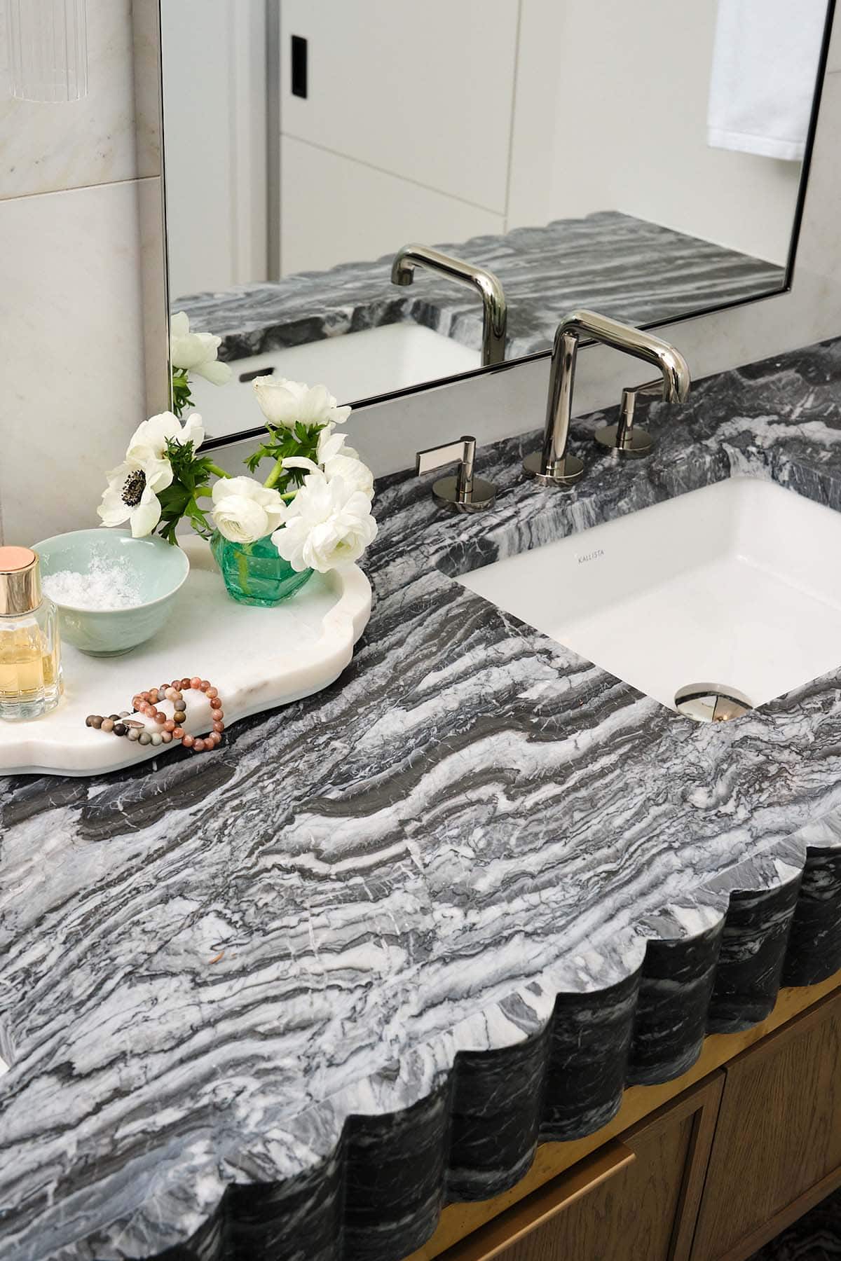 Bathroom vanity detail with dramatic scallop-edged dark marble countertop and polished nickel faucet