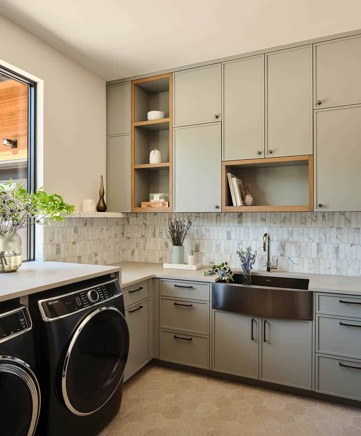 Luxury laundry room with sage green cabinetry, marble mosaic backsplash, black farmhouse sink, and GE washer dryer
