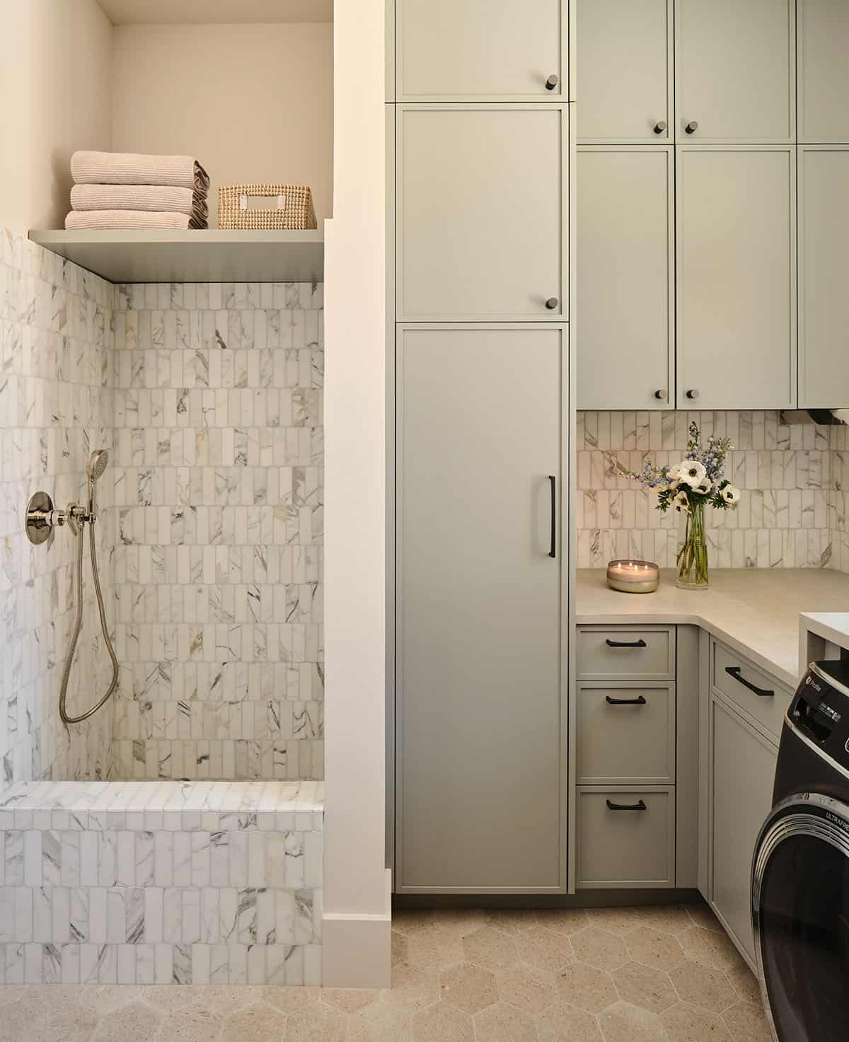 Laundry room dog wash station with marble mosaic tile walls, handheld shower, and sage green cabinetry
