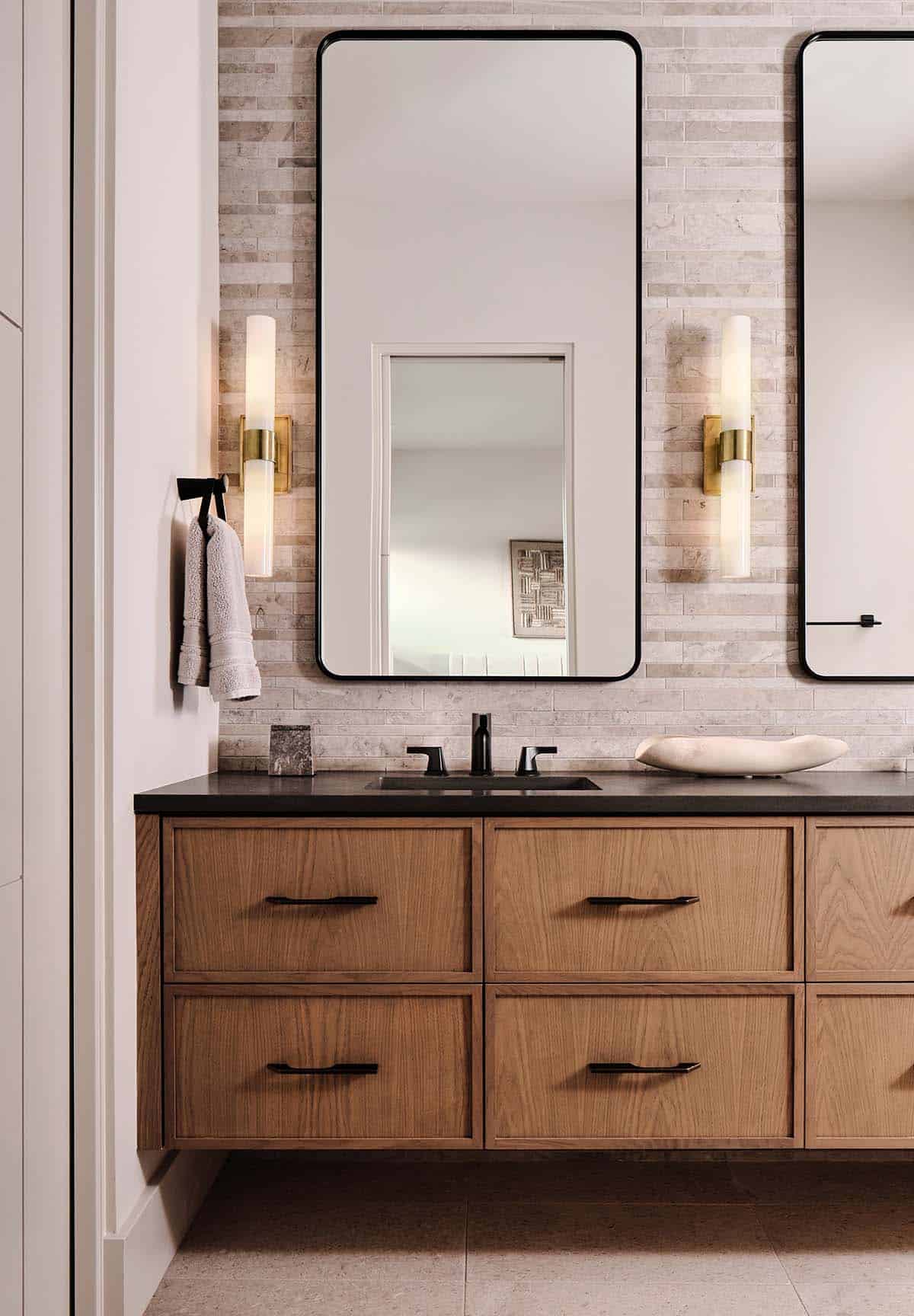Bathroom vanity with oak floating cabinet, dark stone countertop, black matte faucet, and rounded black-framed mirrors