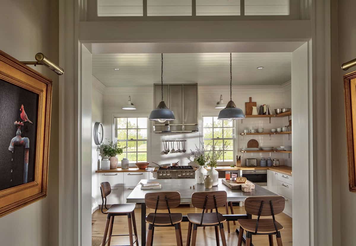 Guest cottage kitchen viewed through doorway with gray pendant lights, white cabinetry, butcher block counters, open shelving, and walnut bar stools