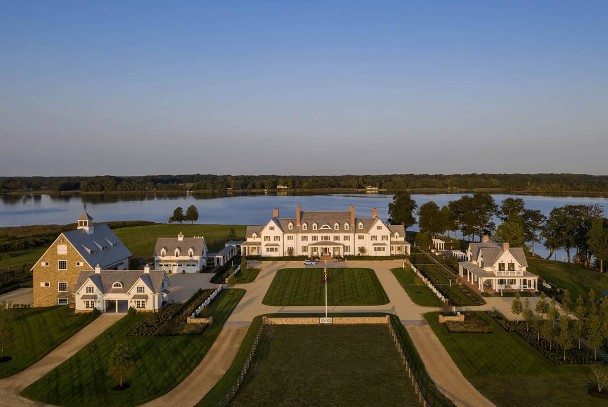 Aerial view of luxury waterfront estate in Maryland with white manor house, stone barn, and guest cottage surrounded by manicured lawns and river