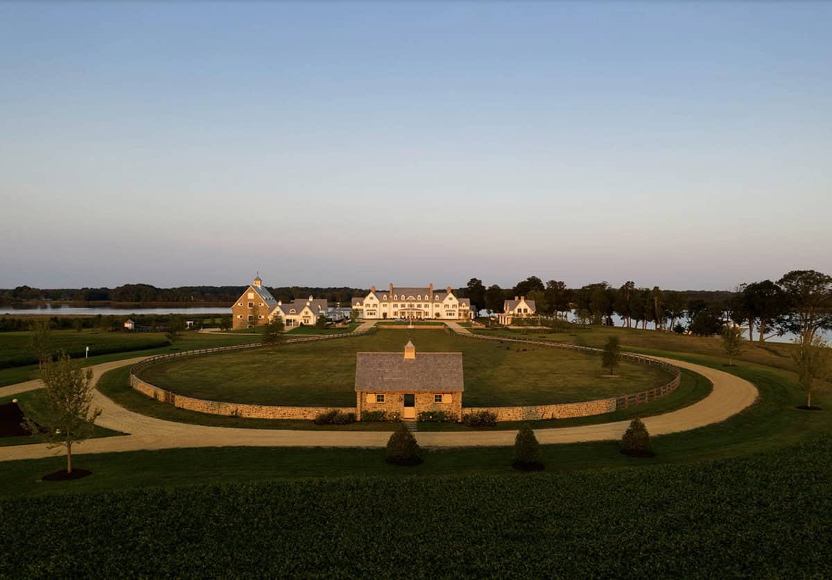 Wide aerial shot of estate at dusk with circular stone paddock and small stone cottage in foreground, manor house and river beyond