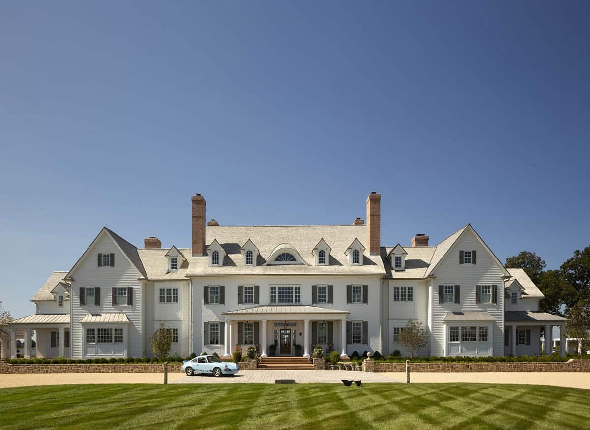 Full front facade of white colonial manor house with light blue vintage Porsche parked on cobblestone forecourt