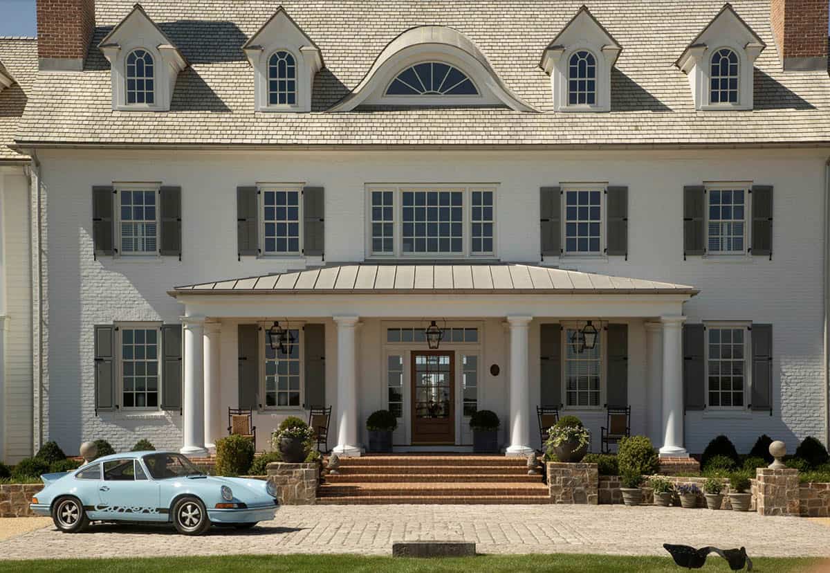  Detail of manor house entrance with columned metal-roof portico, fanlight dormer, gas lanterns, and classic Porsche Carrera