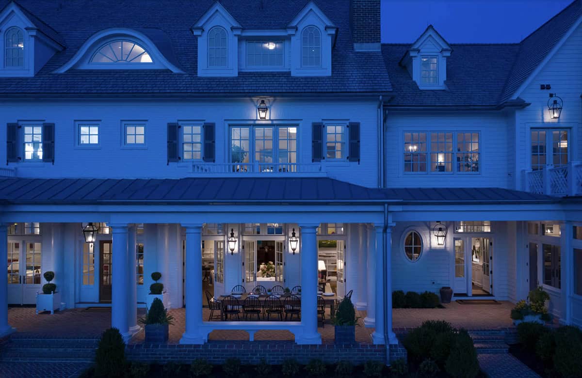 Night view of rear facade with illuminated colonnaded loggia, outdoor dining table, and glowing interior rooms