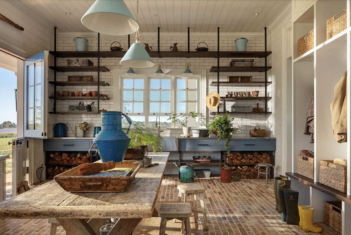 Charming potting room with subway tile walls, open wood shelving, brick floor, farmhouse sink, and blue pendant lights