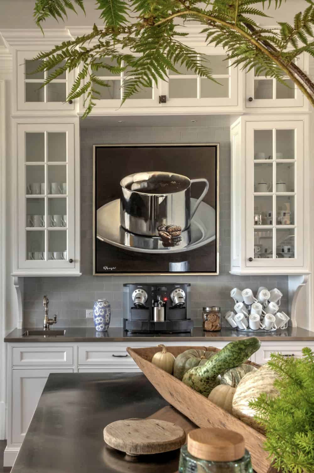 Kitchen coffee station with white glass-front cabinets, gray subway tile backsplash, espresso machine, and large coffee cup painting