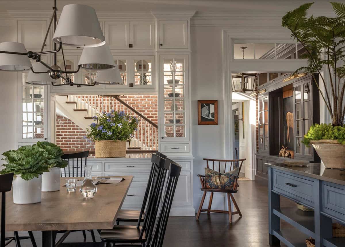 Kitchen and dining area with white cabinetry, exposed brick stairwell, black Windsor chairs, and view through to the entry hall