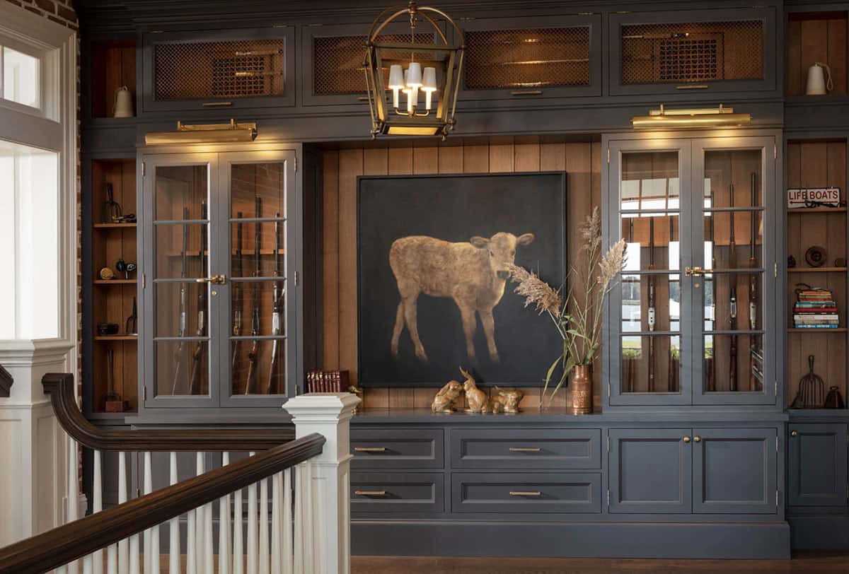 Sporting room with dark built-in gun cabinets, wood-paneled walls, brass lantern pendant, and large calf painting as focal point
