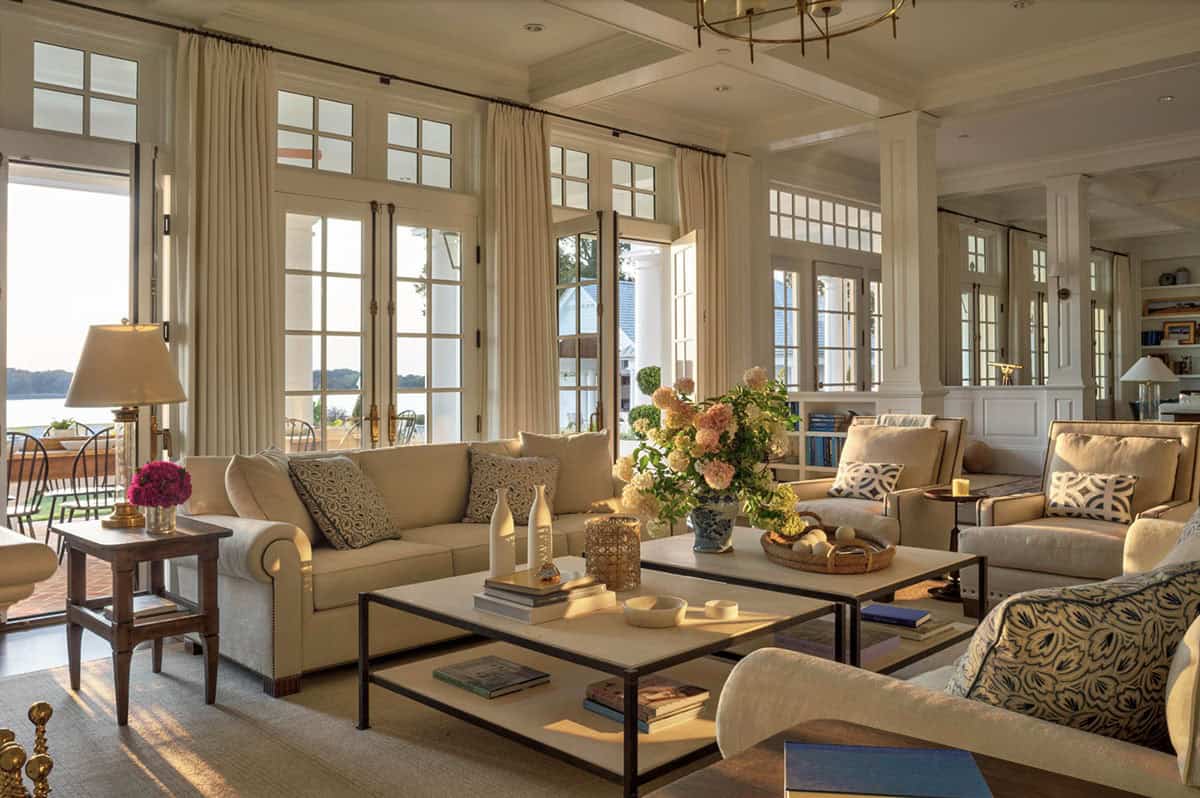 Bright waterfront living room with cream sofas, blue patterned accents, floor-to-ceiling French doors, and river views beyond