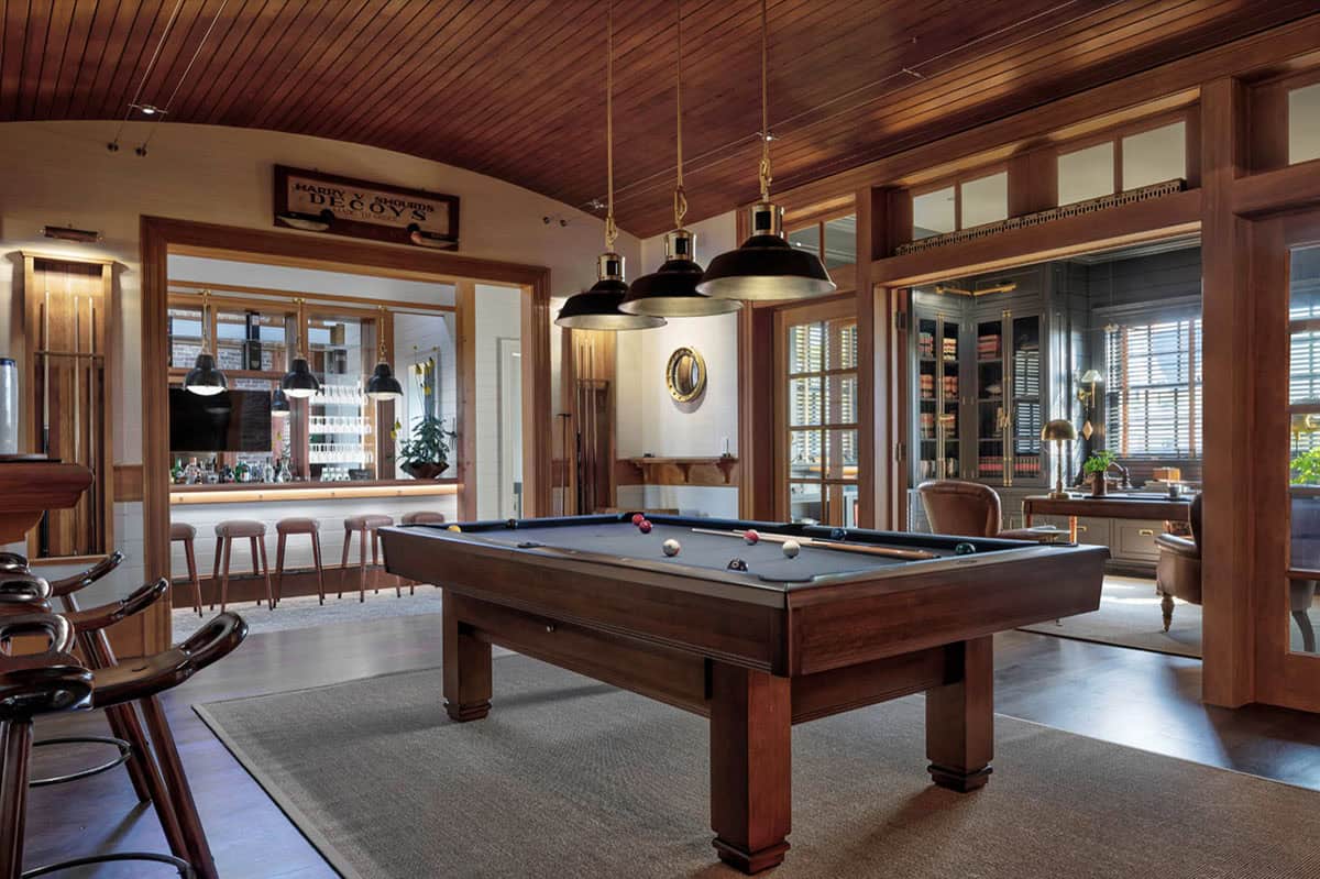 Gentleman's recreation room with billiard table, vaulted wood ceiling, brass pendant lights, full bar, and adjacent study