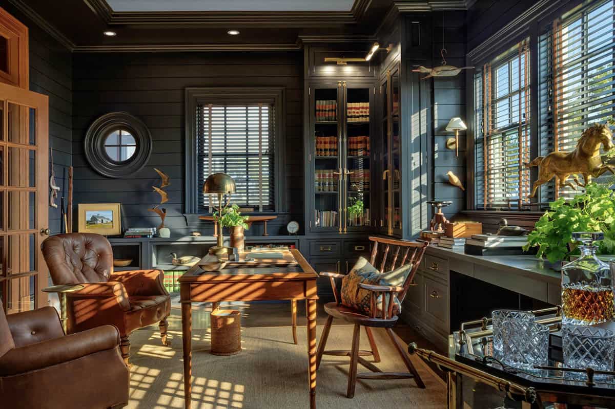 Dark navy home office with leather chairs, wooden writing desk, glass-front bookcase, porthole mirror, and brass animal sculptures