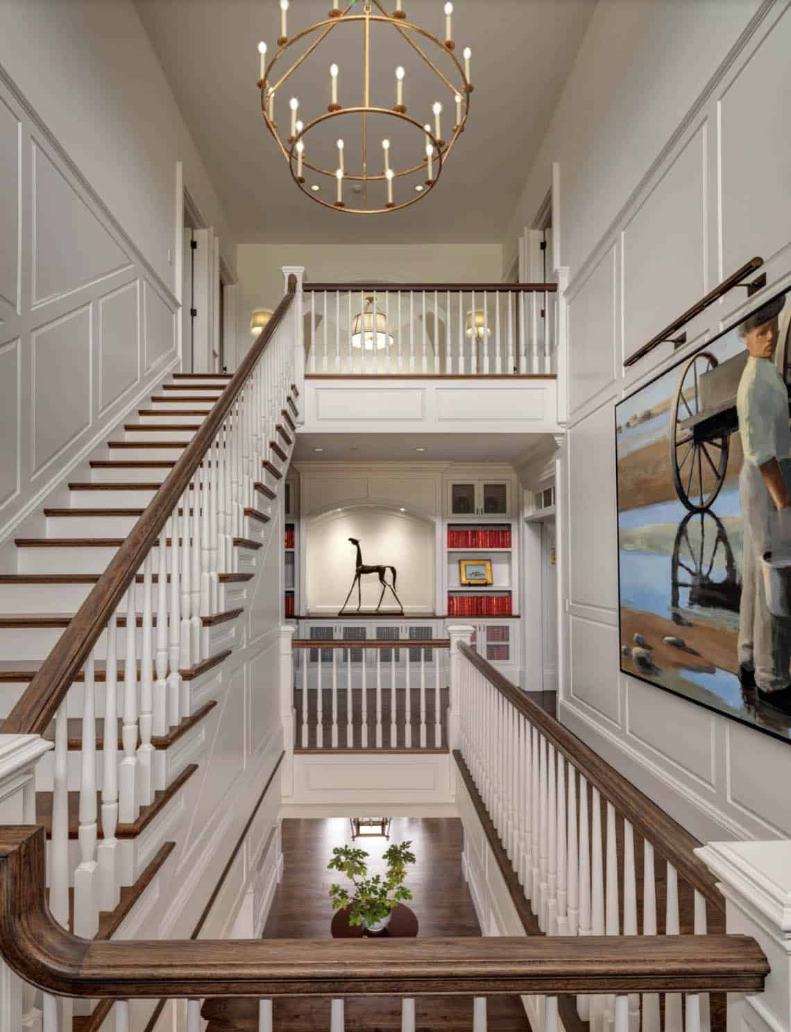 Grand double staircase foyer with dark wood handrails, white balusters, brass candle chandelier, and horse sculpture in arched niche
