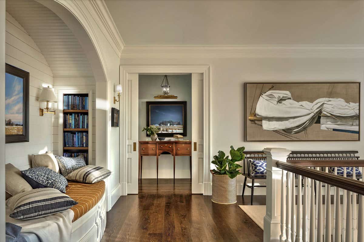 Upper landing with built-in arched window seat, bookshelves, nautical painting, and view through doorway to antique writing desk