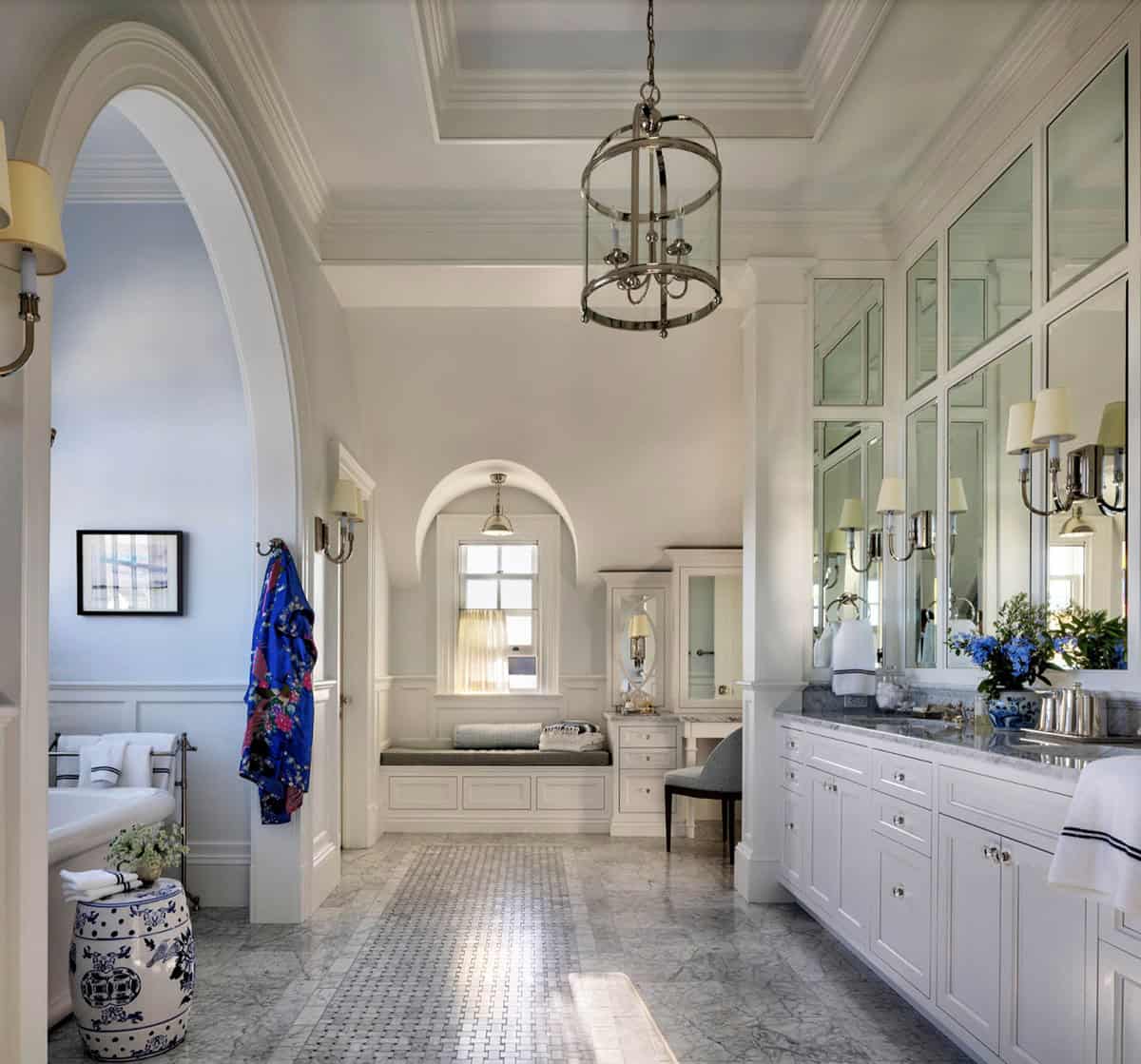 Luxurious primary bathroom with marble mosaic floor, arched doorways, wall-to-wall mirrored vanity, polished nickel lantern, and soaking tub alcove