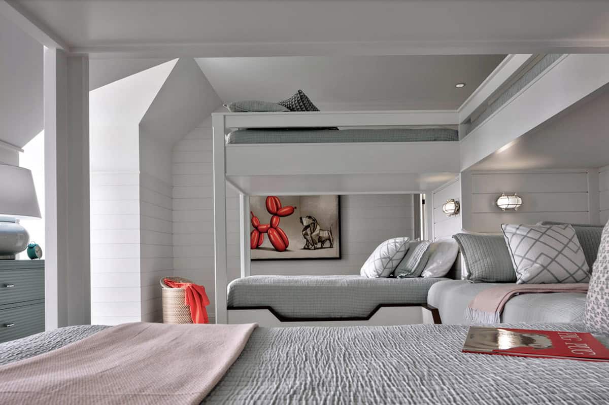 Children's bunk room with built-in triple bunk beds, shiplap walls, porthole sconces, gray bedding, and colorful balloon dog artwork