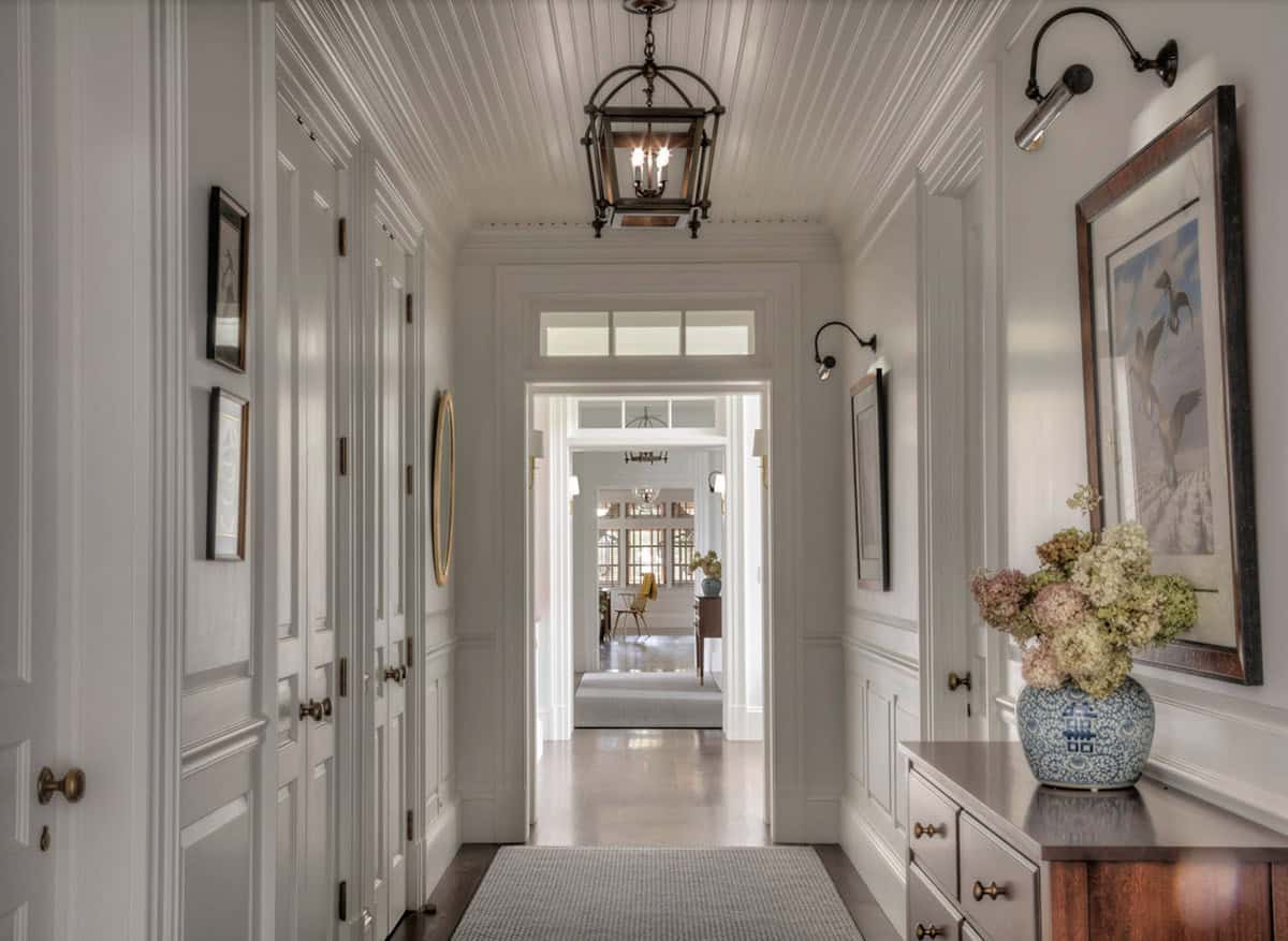 Entry hallway with beadboard ceiling, bronze lantern pendant, paneled doors, duck print artwork, and blue-and-white ginger jar on a wood chest