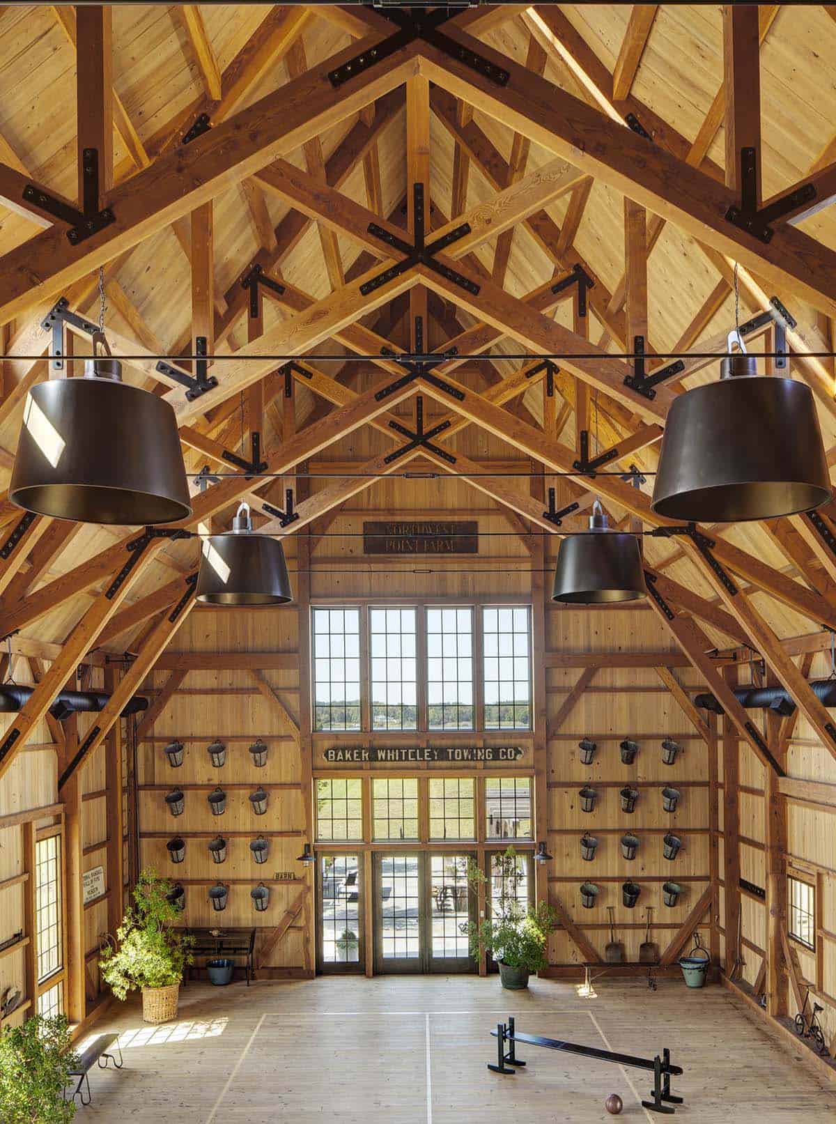 Interior of timber-frame entertainment barn with soaring exposed truss ceiling, large industrial pendants, and antique signage wall