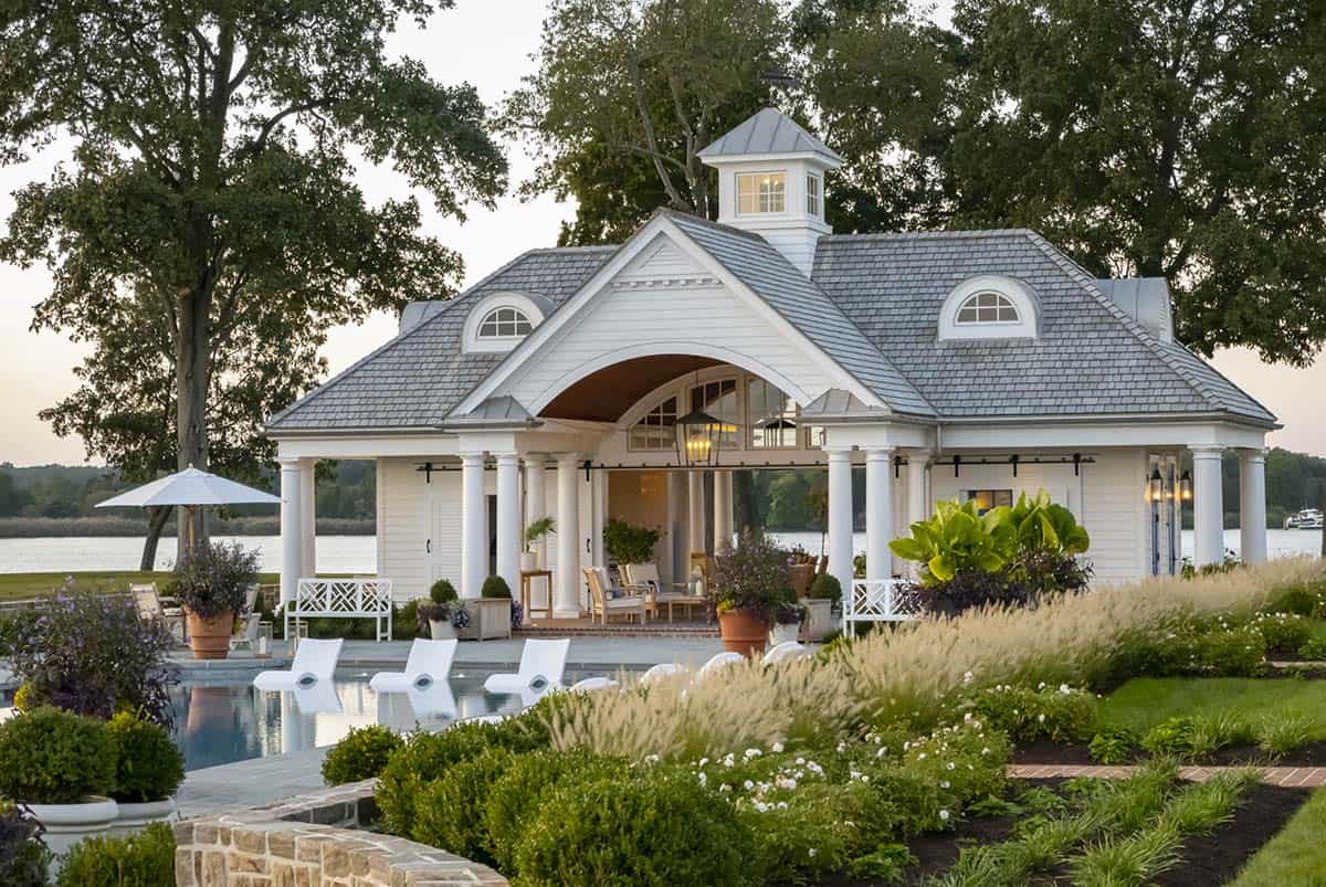 Pool house at golden hour with white colonnade, open arched pavilion, ornamental grasses, lush plantings, and pool in foreground
