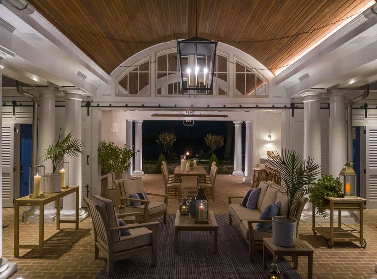 Illuminated pool house pavilion at night with barrel-vaulted cedar ceiling, black lantern pendant, teak furniture, and candles