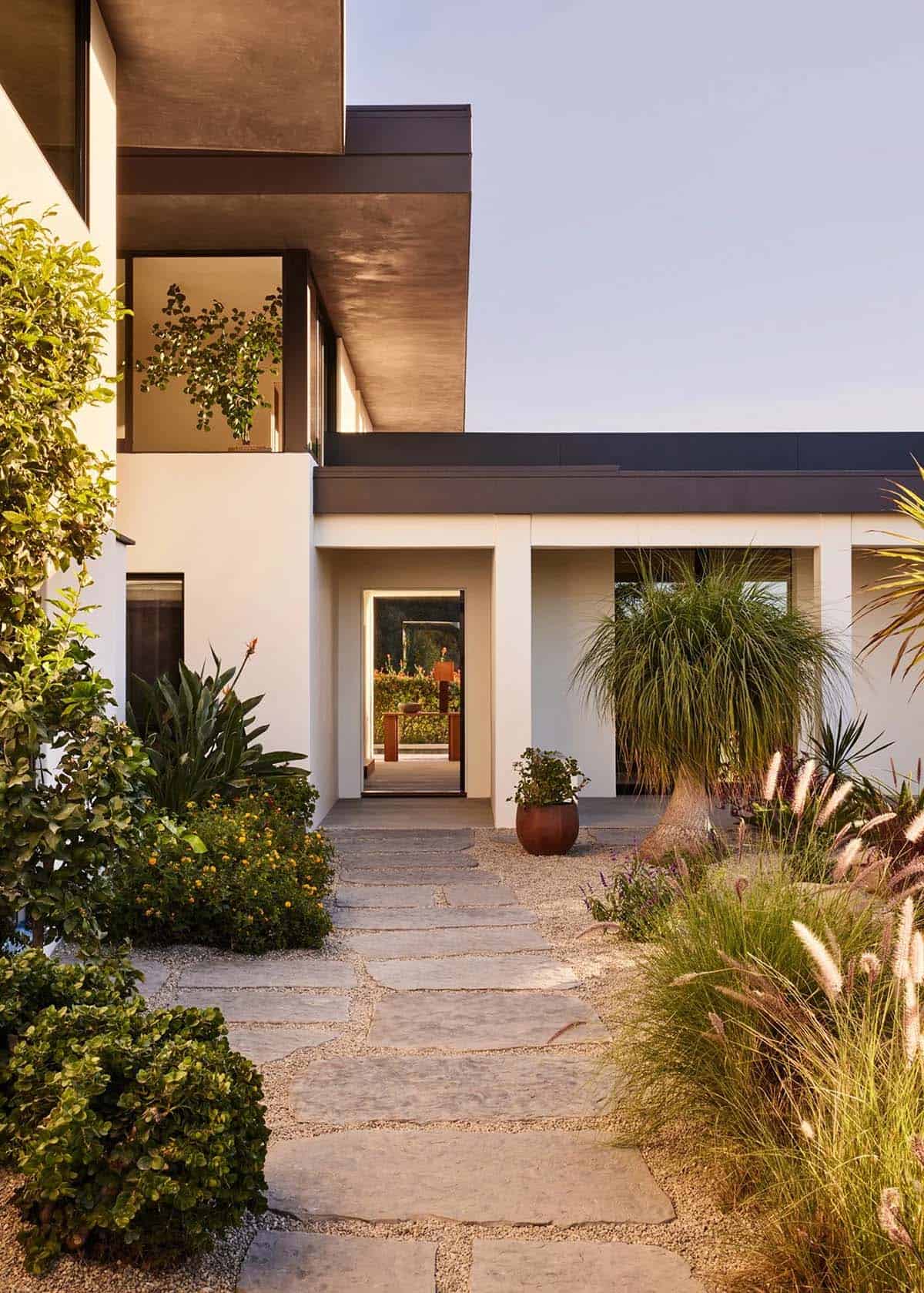 Modern California home entry with stucco exterior, flat roof, stone path, and lush landscaping