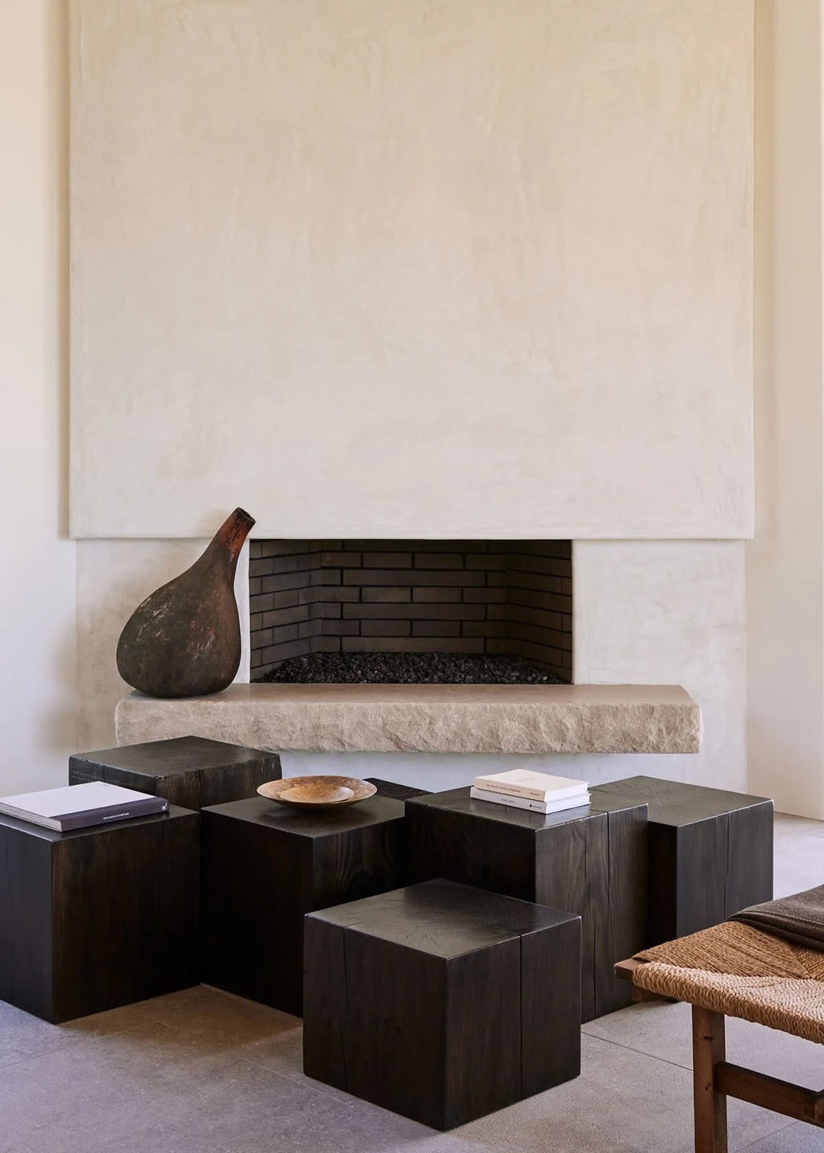 Minimalist plaster fireplace with rough stone hearth, dark wood cube tables, and ceramic vase