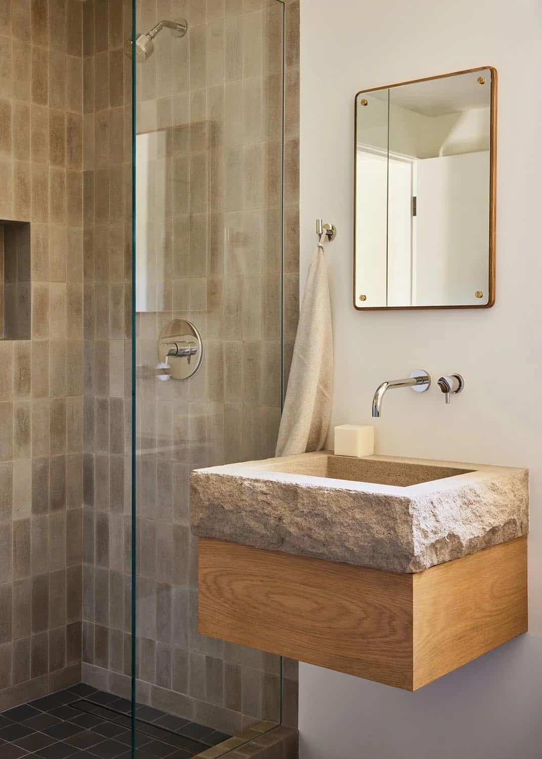 Bathroom with chiseled stone vessel sink on oak vanity, warm tile shower, and wood-framed mirror