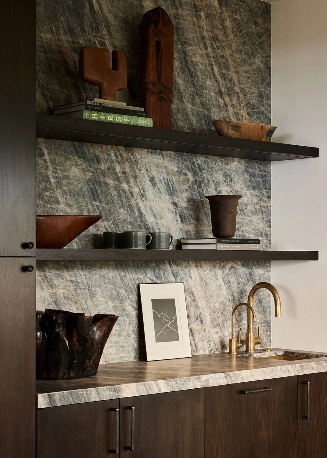 Dark butler's pantry with dramatic stone slab backsplash, open shelves, brass faucet, and artisan objects