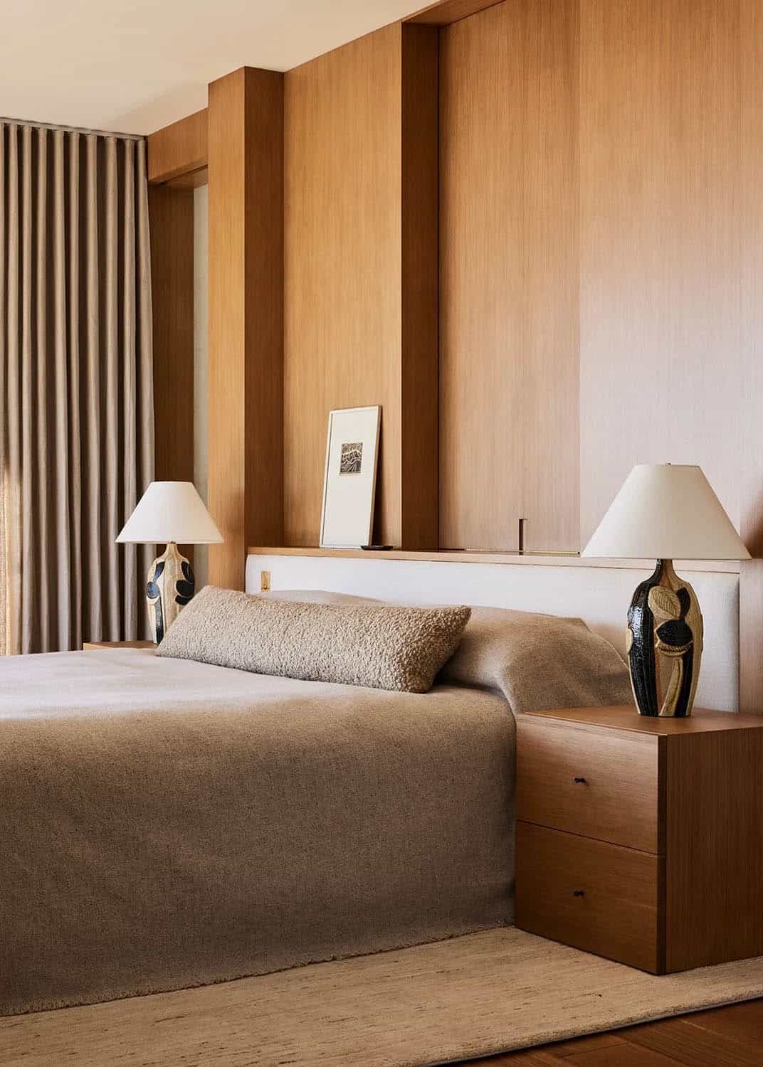 Primary bedroom with floor-to-ceiling wood paneling, upholstered headboard, ceramic lamps, and linen drapes