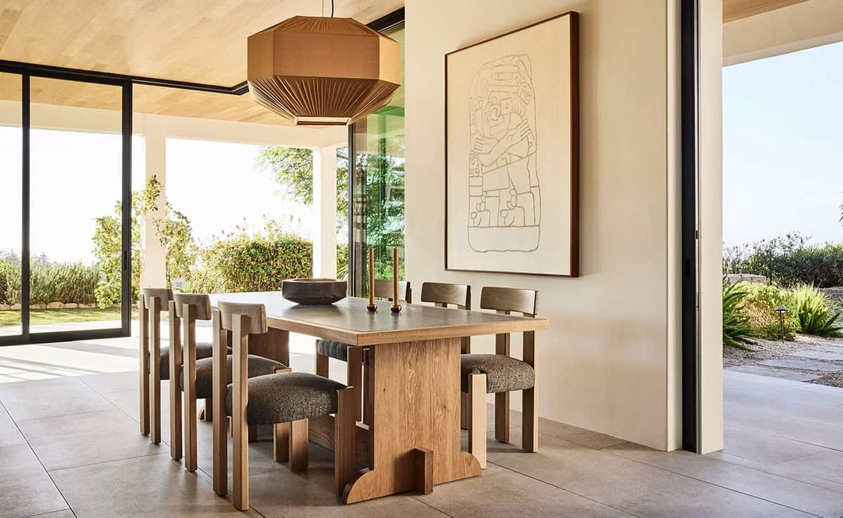 Dining room with oak pedestal table, sculptural chairs, large wall art, and garden views through glass doors