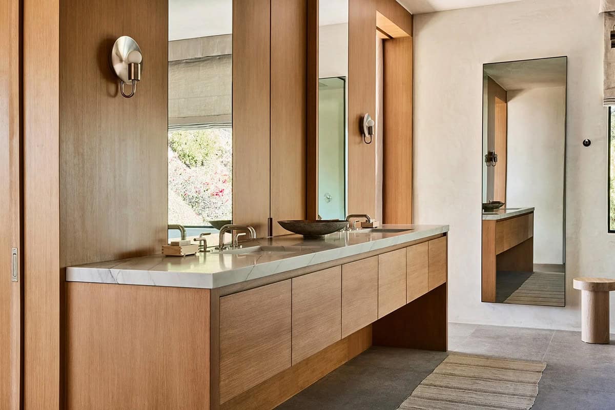 Primary bathroom with oak double vanity, marble countertop, vessel sinks, and tall mirror panels
