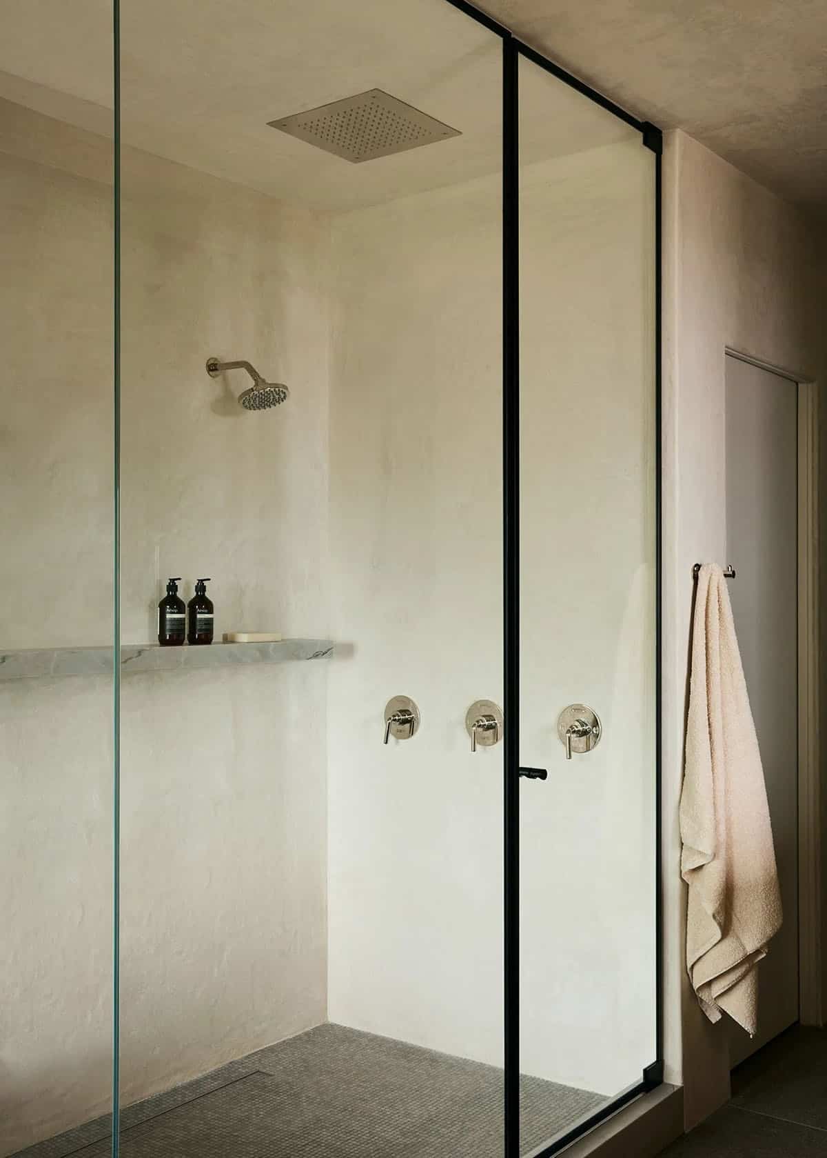 Walk-in shower with rain head, wall-mount fixtures, marble shelf, and black-frame glass door