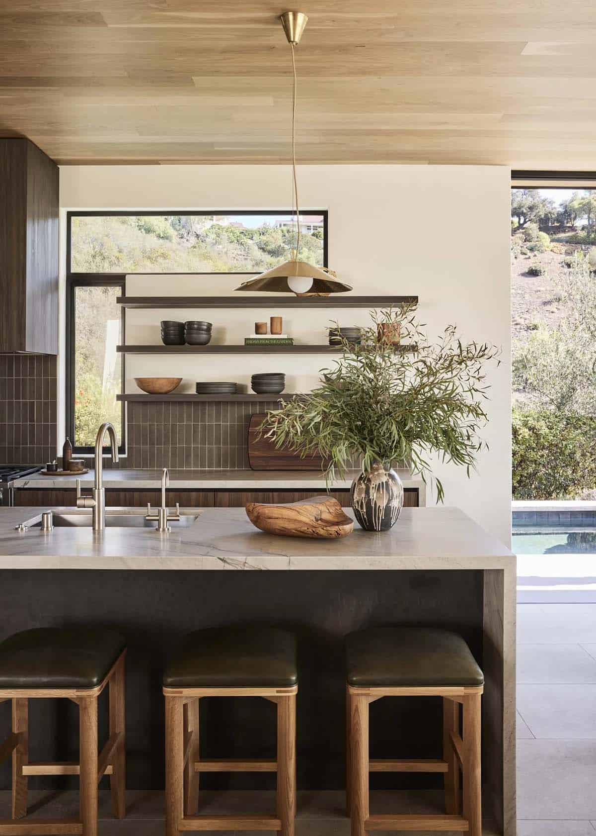 Kitchen island with marble countertop, green leather bar stools, open shelving, and brass pendant light