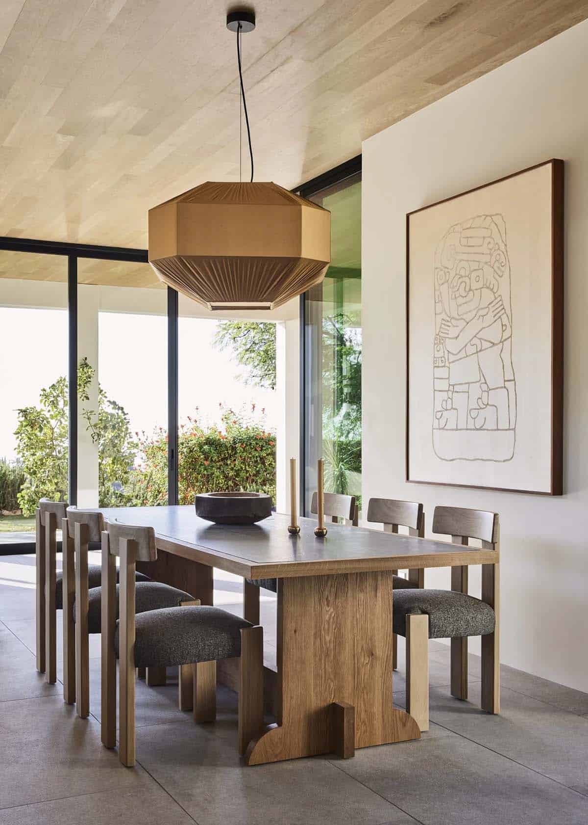 Dining room with oak pedestal table, sculptural chairs, oversized woven pendant, large framed artwork, and garden views