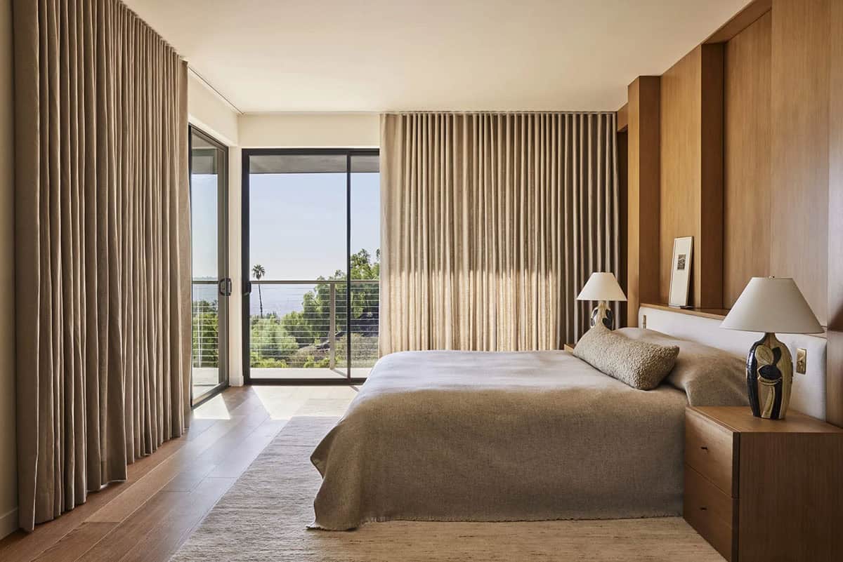 Primary bedroom with wood paneling, floor-to-ceiling linen drapes, ceramic lamps, and balcony with ocean views