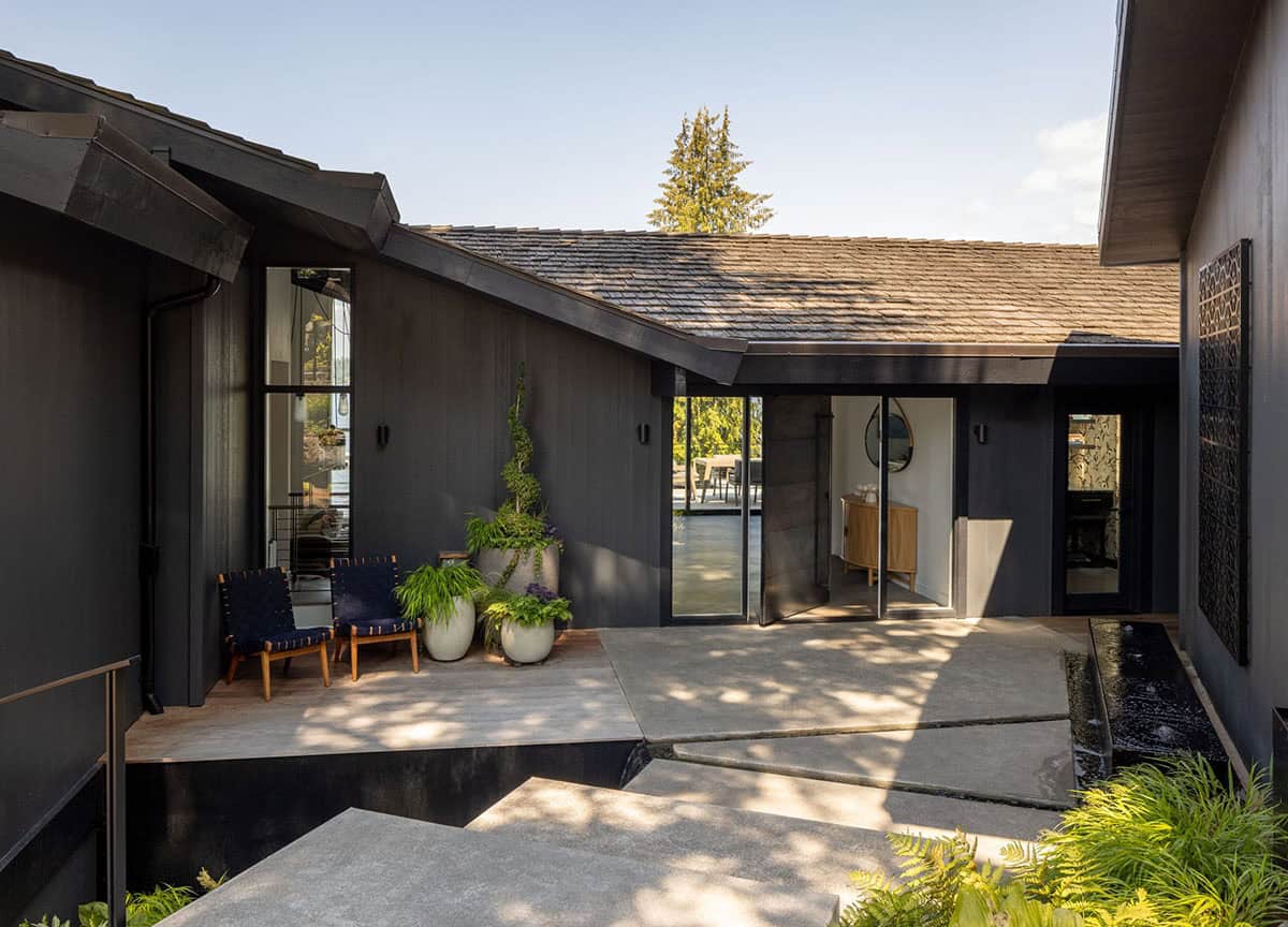 Mid-century modern courtyard entry with dark siding, concrete pavers, water feature, and potted plants