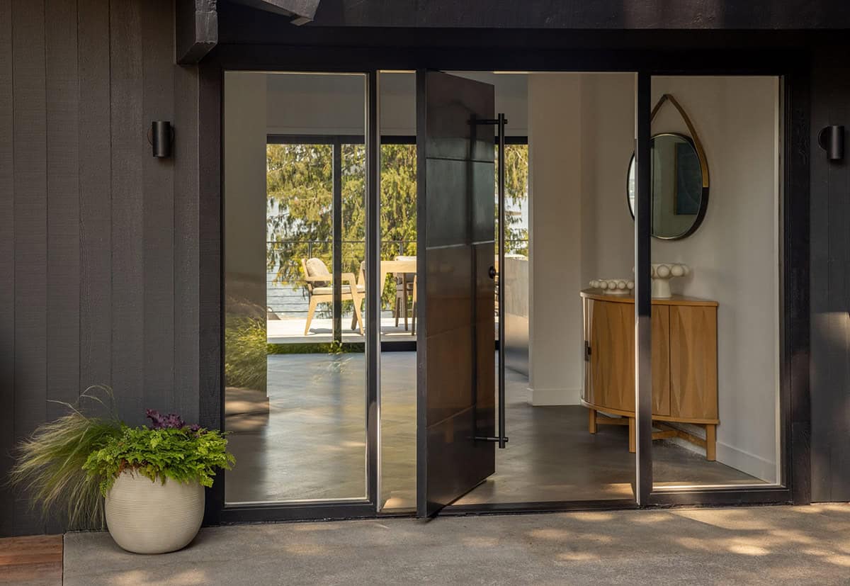 Mid-century modern pivot glass entry door with dark frame, round mirror, and oak cabinet in foyer