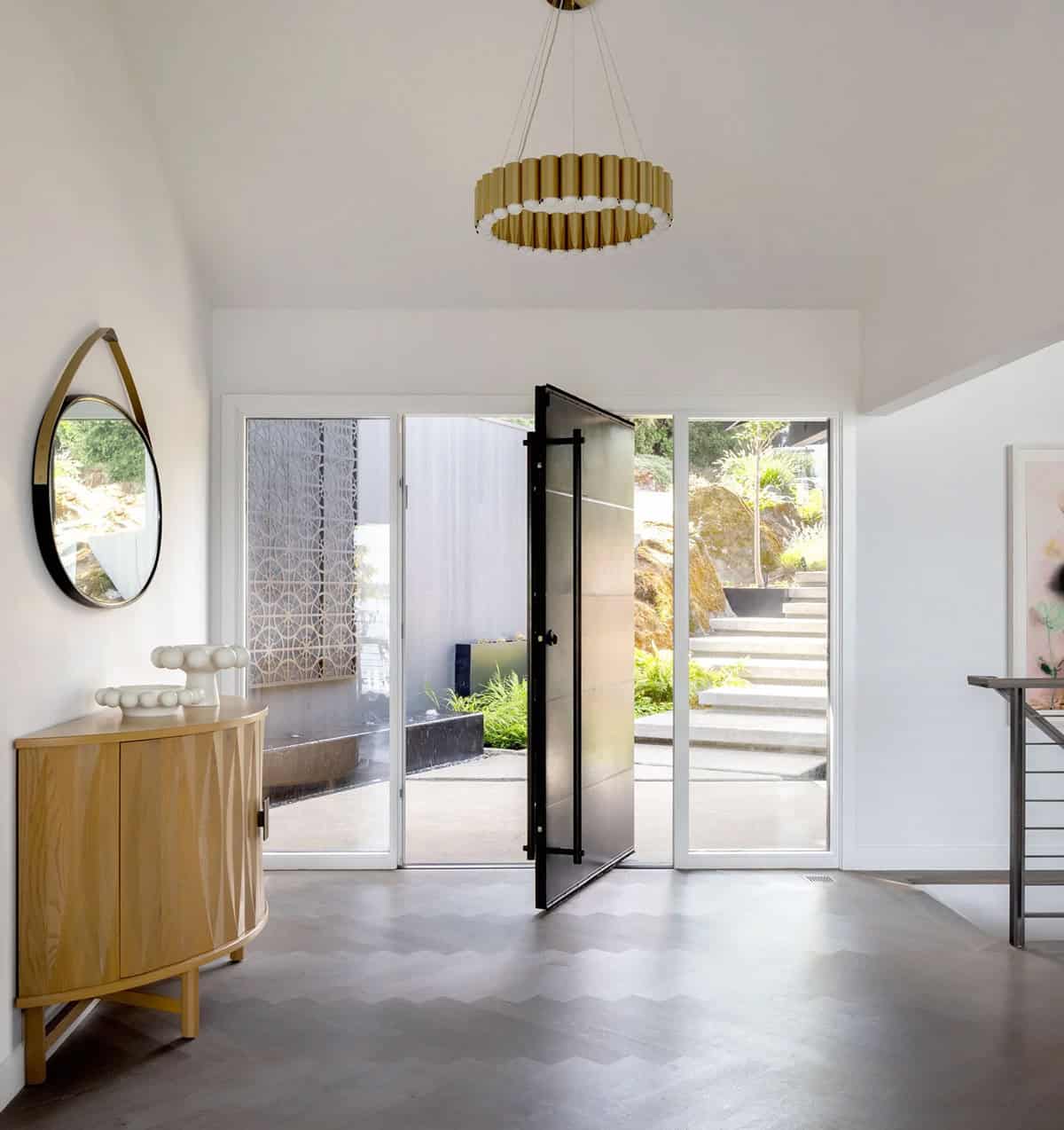 Bright foyer with brass drum chandelier, pivot glass door, chevron floor, and oak console cabinet