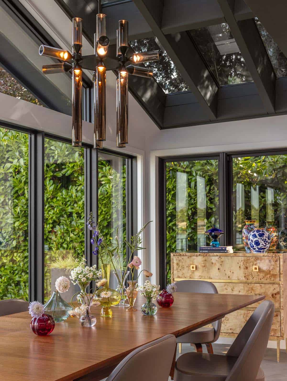 Dining room with chrome Sputnik chandelier, skylight, burl wood credenza, and colorful glass vases